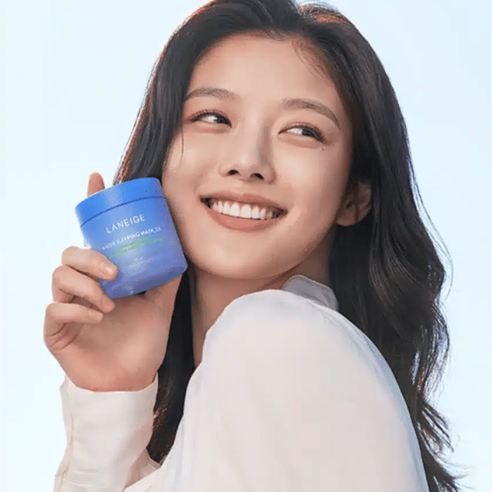 Leende kvinna håller upp en blå burk av LANEIGE Water Sleeping Mask framför ljusblå bakgrund.