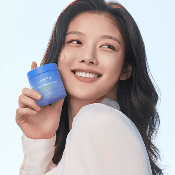 Leende kvinna håller upp en blå burk av LANEIGE Water Sleeping Mask framför ljusblå bakgrund.