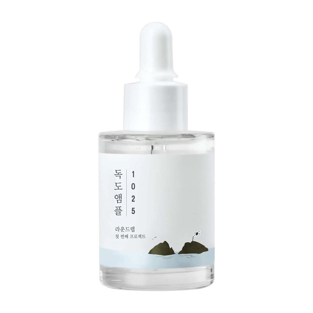 Uma garrafa transparente com 1025 Dokdo Ampoule soro facial, decorada com tema marítimo minimalista, sobre fundo branco.