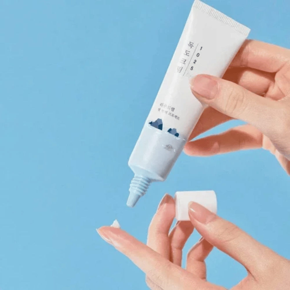 Round Lab 1025 Dokdo Eye Cream tubo com creme leve aplicado na ponta do dedo para cuidado suave da pele sensível à volta dos olhos