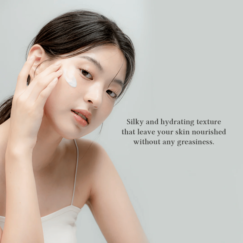 A imagem mostra uma mulher aplicando um creme de pele no rosto. O texto na imagem descreve o produto como sedoso e hidratante, e enfatiza que nutre a pele sem deixar uma sensação oleosa. Isso sugere que o creme tem uma textura leve e agradável que é bem absorvida pela pele.