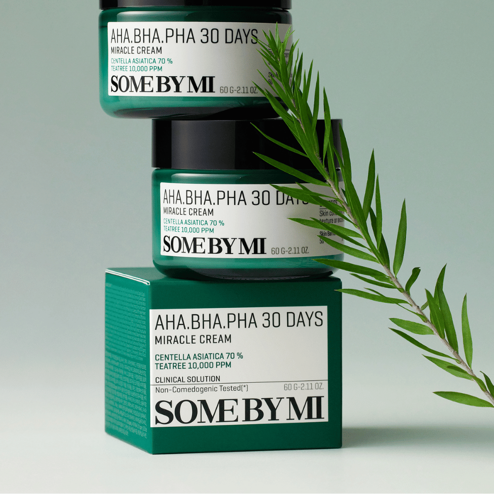 Uma imagem que mostra dois frascos de "SOME BY MI AHA, BHA, PHA 30 Days Miracle Cream" empilhados sobre uma caixa de tom verde. O creme, que é rico em centella asiatica e óleo de tea tree, é desenhado para melhorar a qualidade da pele e aliviar problemas de pele. Atua hidratando e acalmando.