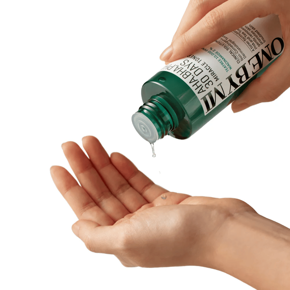 Uma mão segura uma garrafa verde com o texto "AHA, BHA, PHA 30 Days Miracle Toner" e espreme um líquido claro na palma da outra mão, pronto para uso.