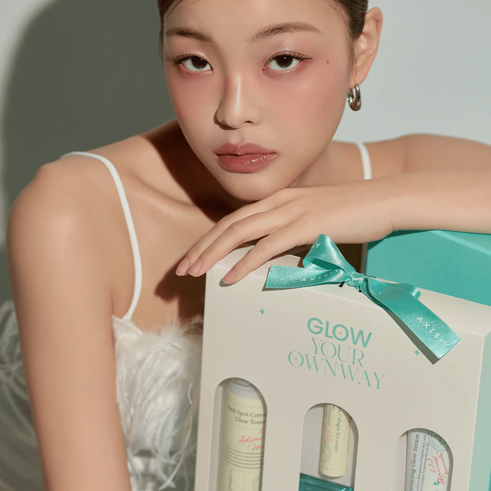 Modelo com maquiagem elegante segurando a caixa de presente “Glow Your Own Way” da AXIS-Y – um Kit de cuidados com a pele elegante, perfeito como presente para si mesmo ou para alguém de quem gosta.