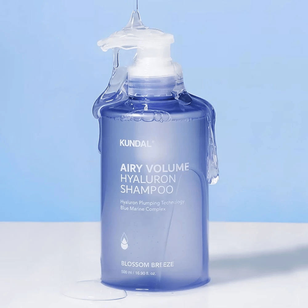 KUNDAL Airy Volume Hyaluron Shampoo Blossom Breeze em frasco de bomba azul, com ácido hialurônico e Complexo Blue Marine, fotografado com água corrente.