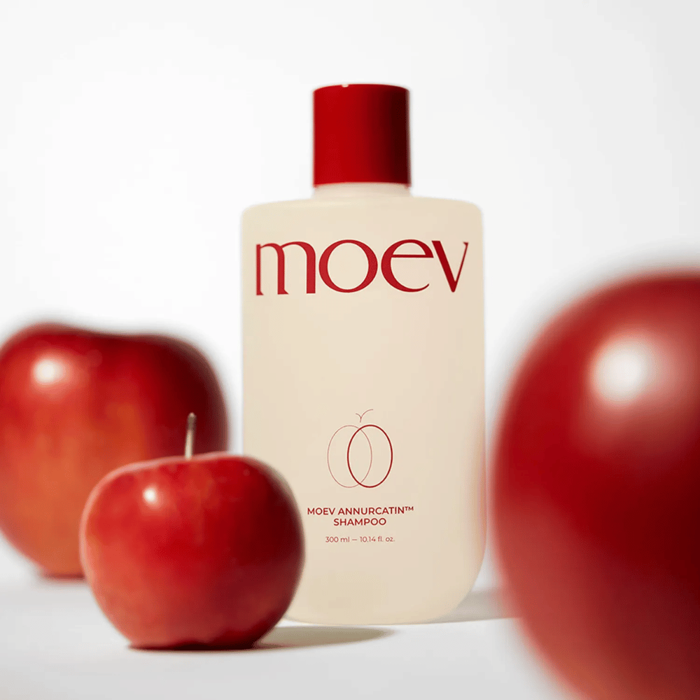MOEV Annurcatin Shampoo colocado entre maçãs vermelhas – inspirado nos antioxidantes da maçã Annurca que proporcionam cabelo mais forte, saudável e brilhante.