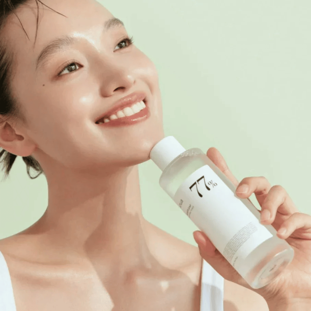 Uma mulher acalma sua pele sensível com uma garrafa Heartleaf 77% Soothing Toner de Anua, contendo extrato de folha de camaleão.