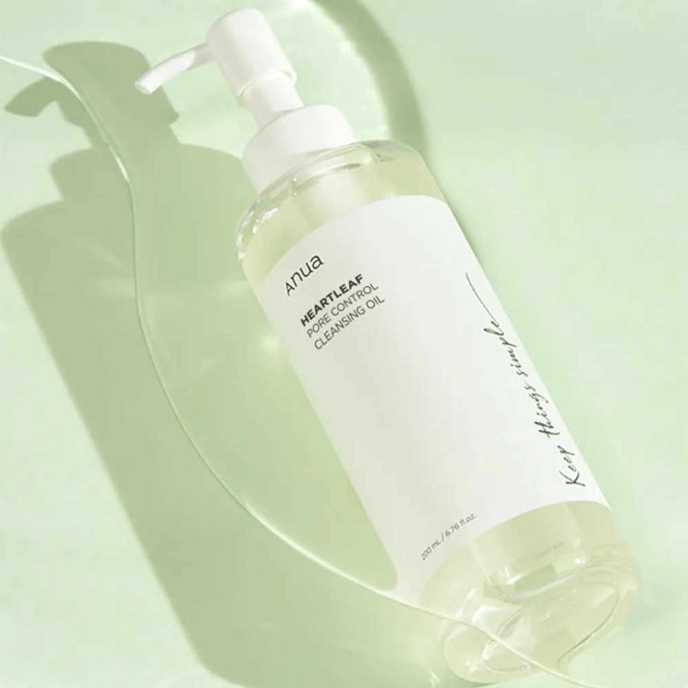Na imagem vê-se ANUA Heartleaf Pore Control Cleansing Oil, um óleo de limpeza com design de bomba. A garrafa é transparente e o conteúdo parece ter uma consistência leve e oleosa. O rótulo exibe o logotipo da marca e o nome do produto em texto simples e elegante, o que contribui para uma sensação de beleza e pureza minimalista. Está escrito "Keep things simple" como parte do design, o que sugere uma filosofia de simplicidade na rotina de cuidados com a pele. A garrafa contém 200 ml de produto.