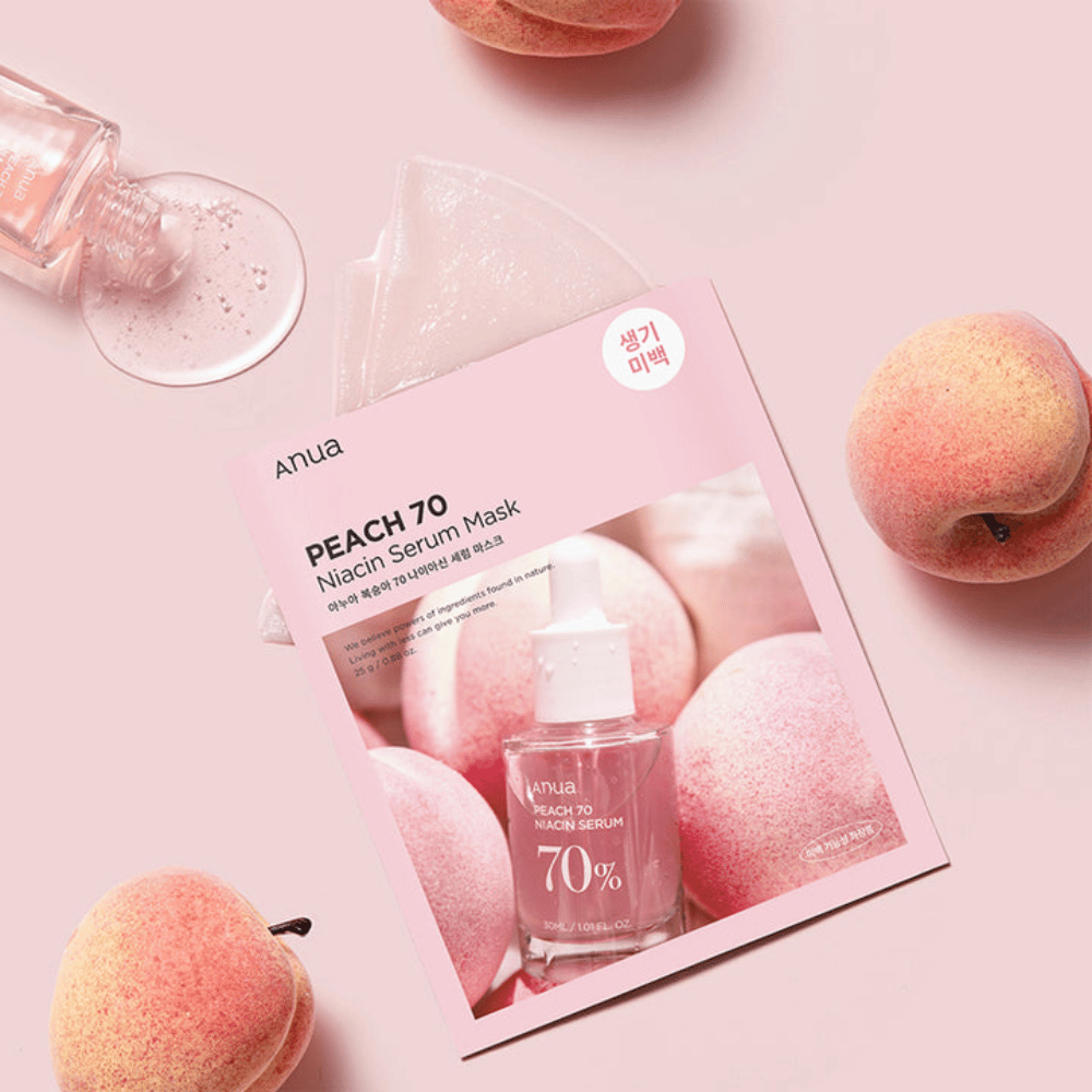 Uma imagem de Anua PEACH 70 Niacin Serum Mask, cercada por pêssegos e um frasco de sérum. A imagem tem um fundo rosa suave, que complementa a embalagem rosa e destaca o produto e os ingredientes.