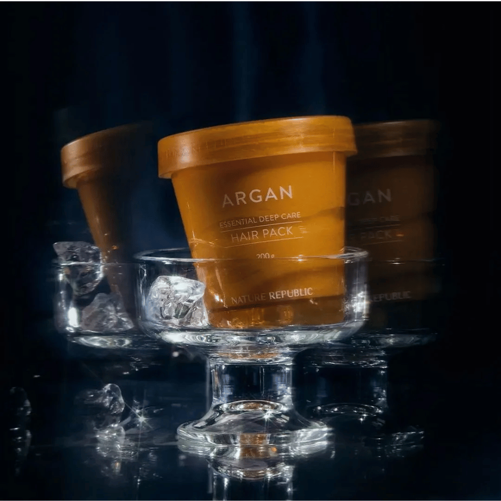 Nature Republic Argan Essential Moisture Repairing Hair Mask colocada em prato de vidro com cubos de gelo – máscara capilar luxuosa e nutritiva.