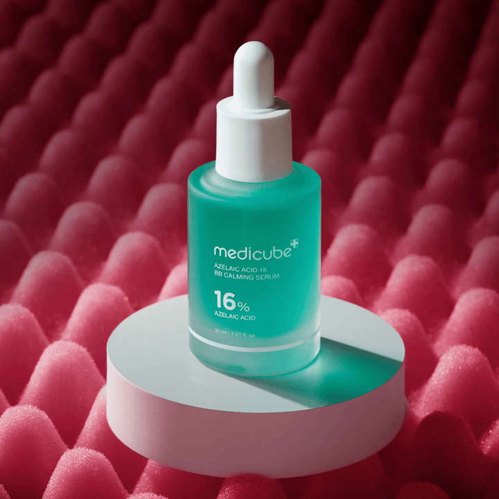 Imagem de produto de Medicube Azelaic Acid 16 BB Calming Serum colocada sobre uma superfície de pódio branca com fundo rosa texturado que realça o perfil calmante e melhorador da pele do sérum.