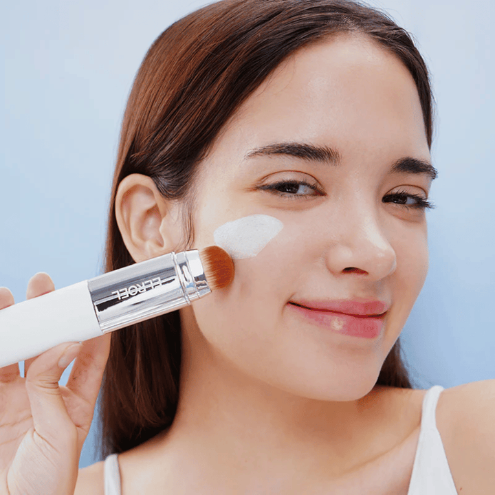 Modelo aplica ELROEL Blanc Cover Cream Stick concealer na bochecha com pincel integrado para cobertura natural e uniforme.