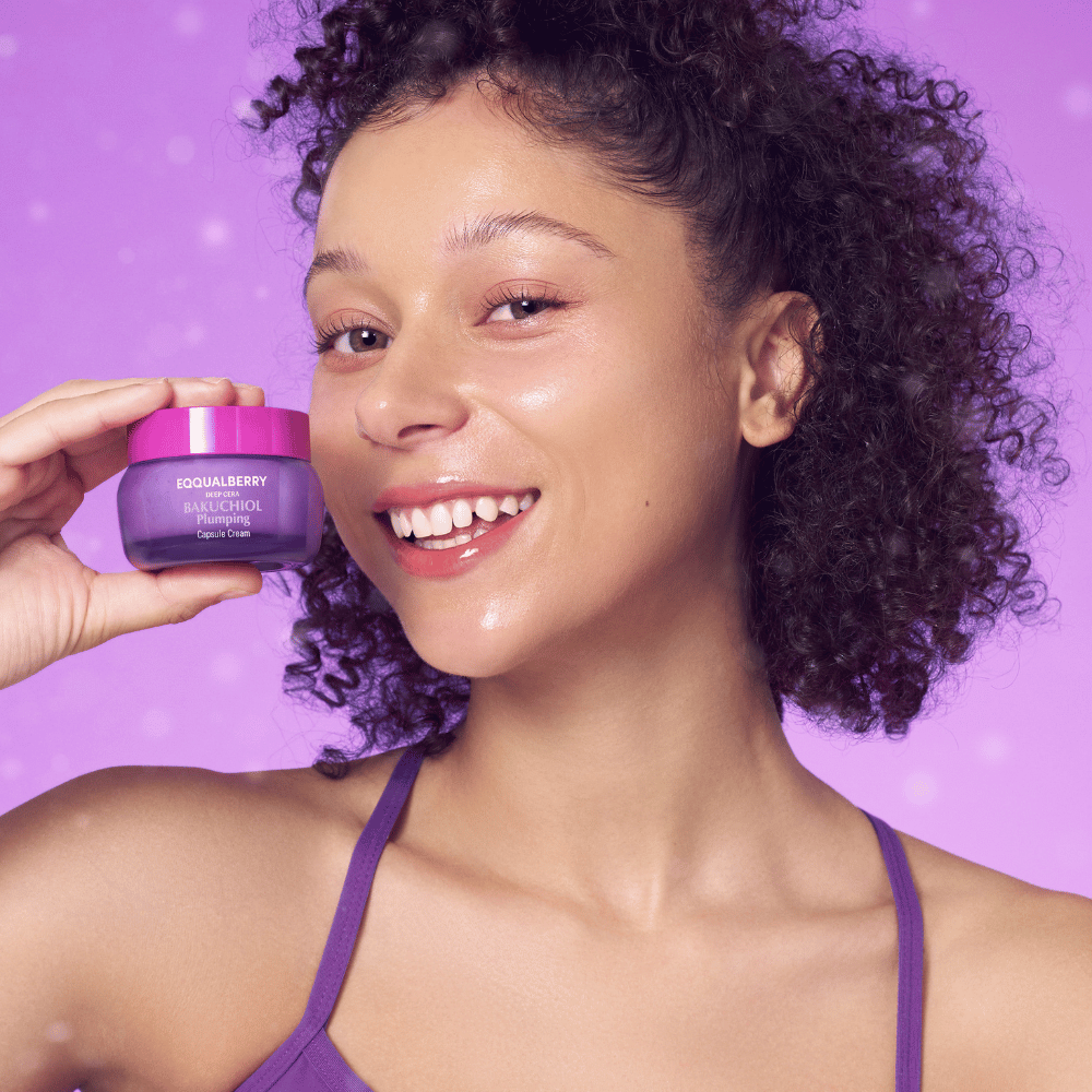 Mulher com pele radiante segura EQQUALBERRY Bakuchiol Plumping Capsule Cream e sorri em frente a um fundo roxo.