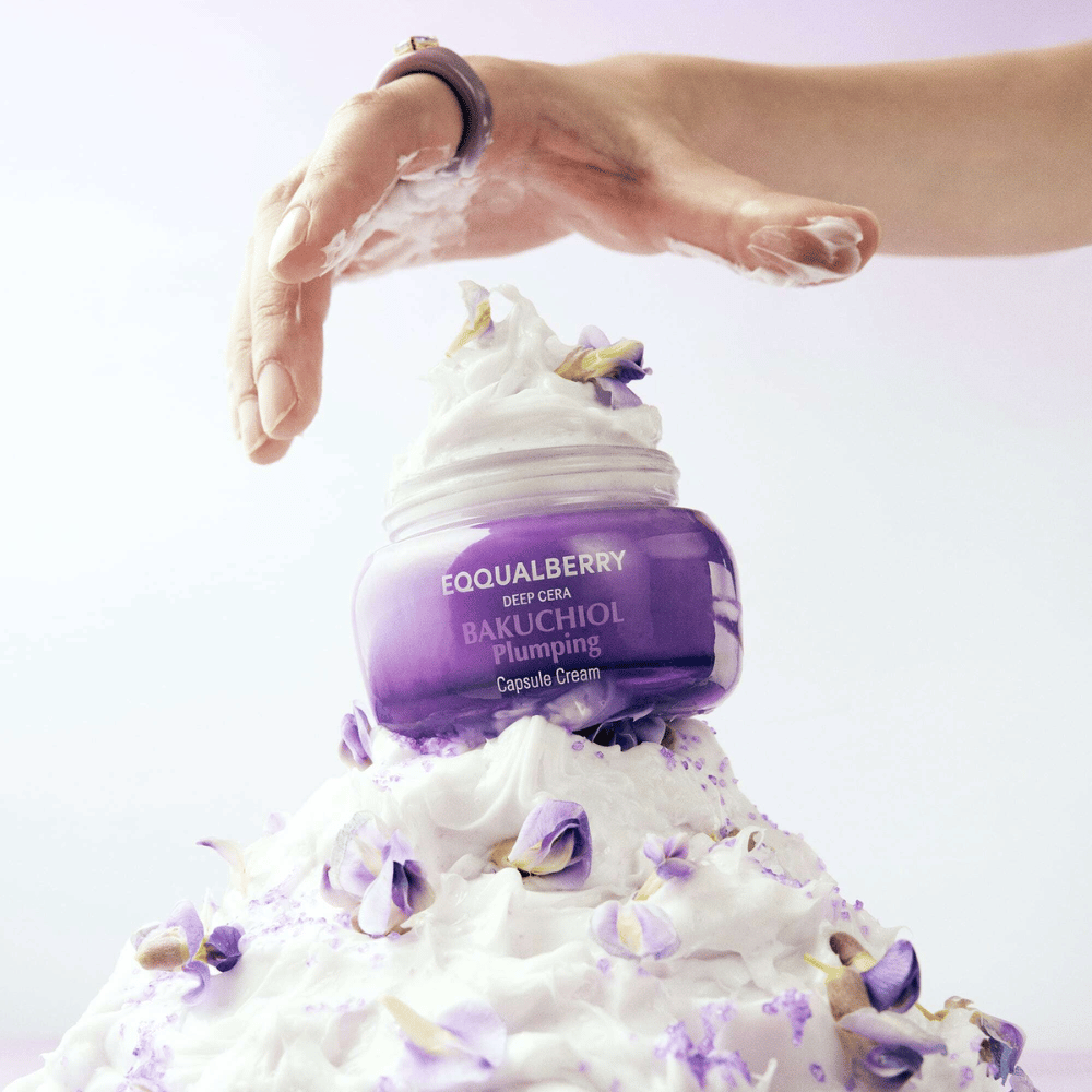 EQQUALBERRY Bakuchiol Plumping Capsule Cream colocado em cima de uma pilha de creme batido com pétalas de flores – simboliza hidratação e cuidado.