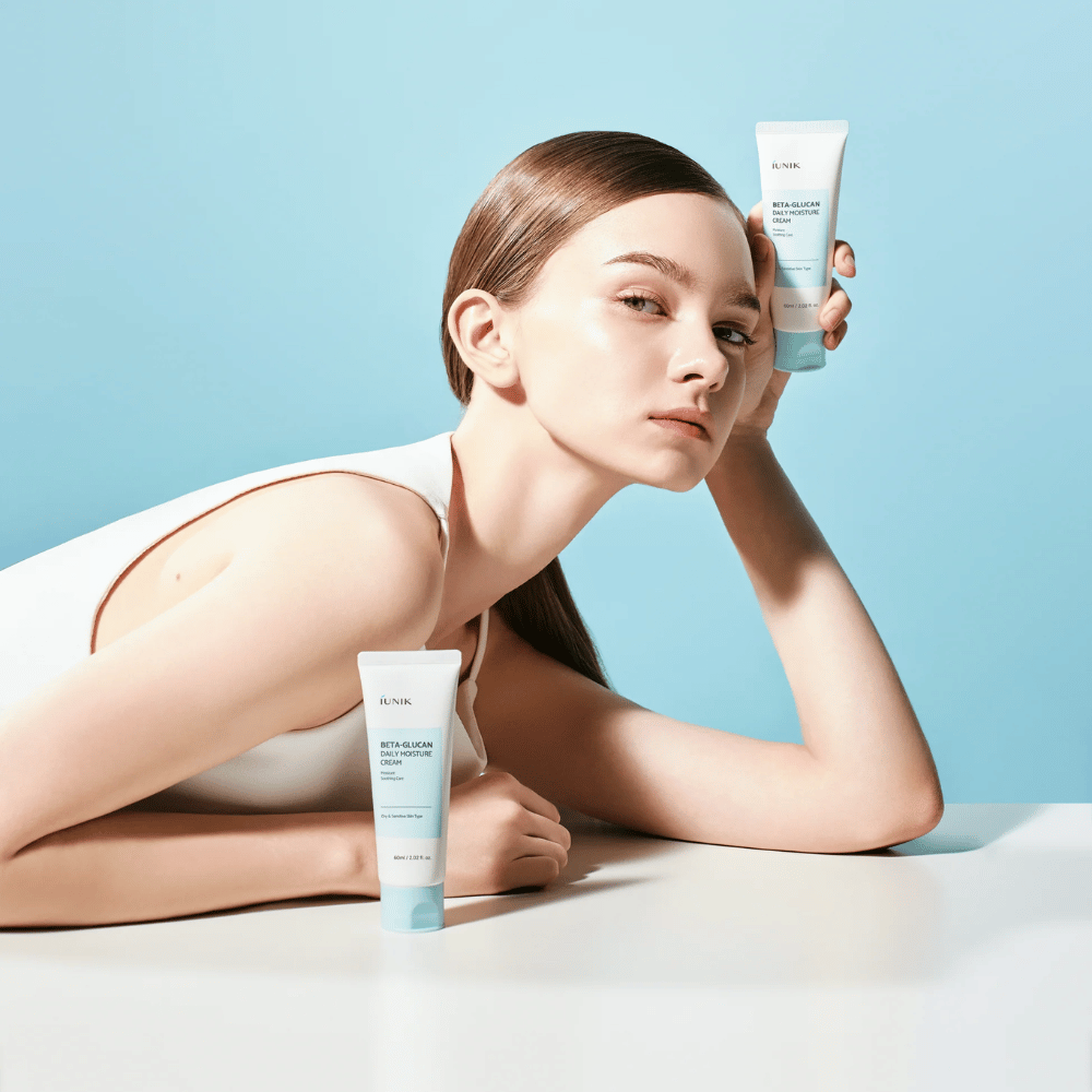 Imagem de estilo de vida em que uma modelo posa com iUNIK Beta-Glucan Daily Moisture Cream sobre um fundo azul-claro. A imagem transmite uma sensação limpa, fresca e hidratante, ao mesmo tempo que o produto é exposto de forma clara.