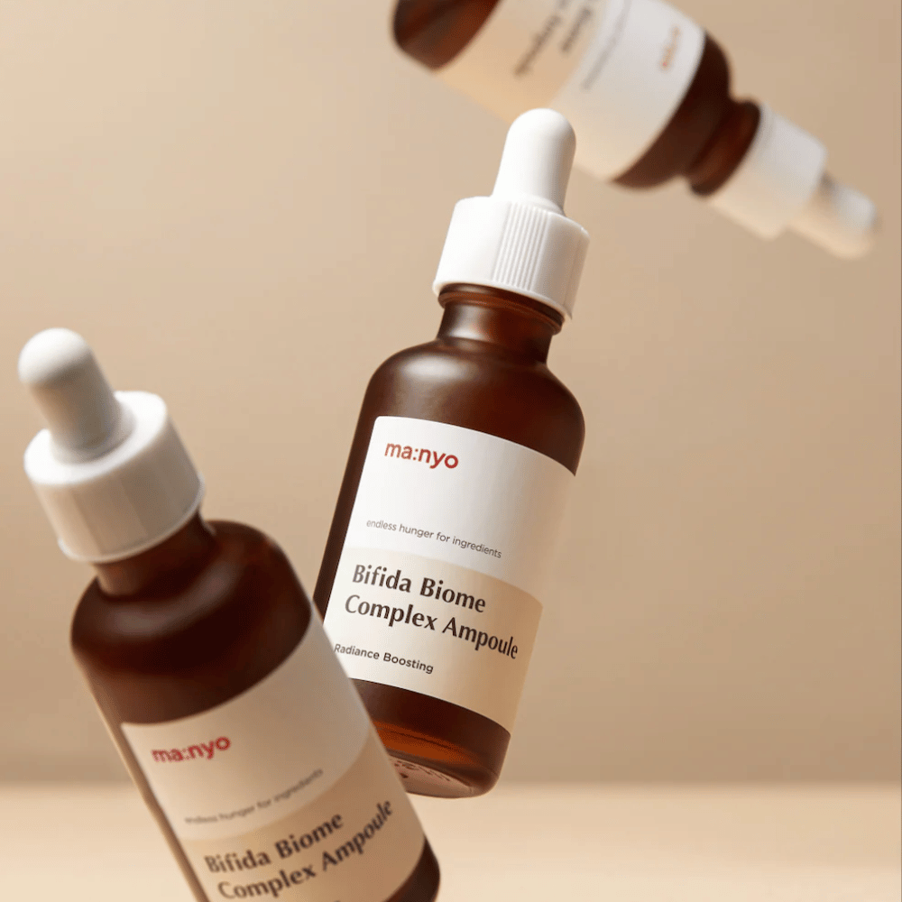 Imagem de produto com vários frascos flutuantes de ma:nyo Bifida Biome Complex Ampoule sobre fundo bege, proporcionando uma sensação moderna e minimalista.