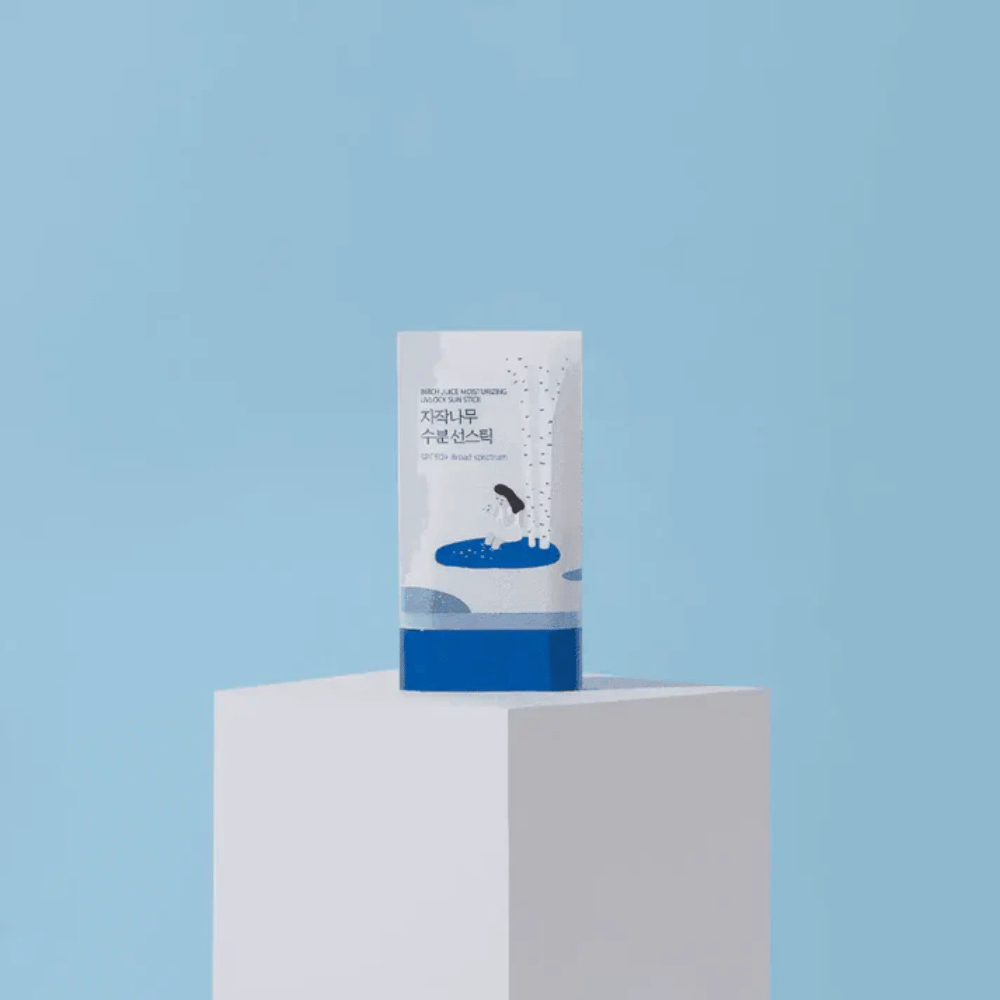 ROUND LAB Birch Juice Moisturizing Sun Stick SPF50+ está sobre um pedestal contra um fundo azul – proteção solar hidratante em stick