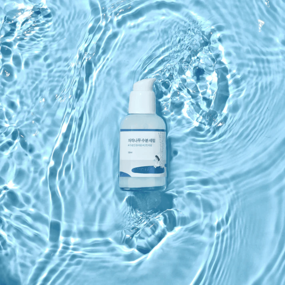 Round Lab Birch Juice Moisturizing Serum em frasco de bomba flutuando em água azul com reflexos de luz solar.