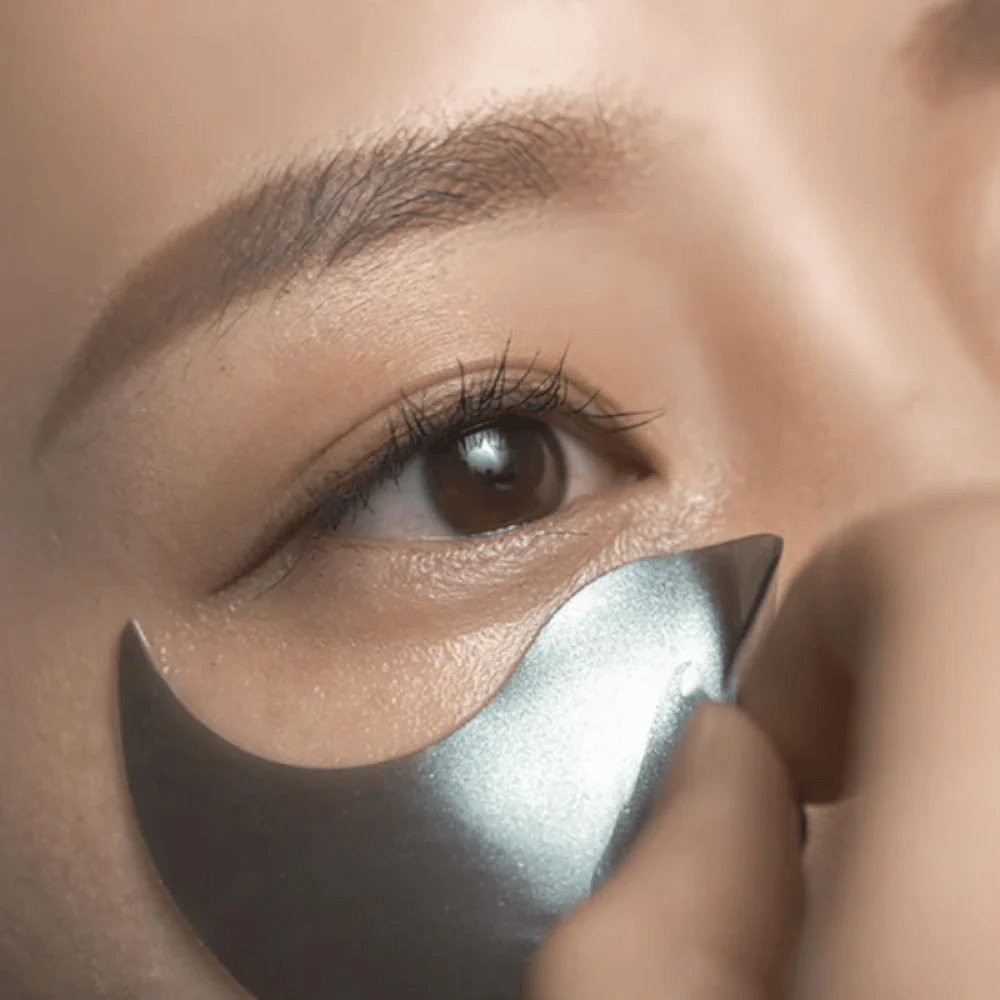 Imagem detalhada em que um patch hidrogel preto para os olhos é aplicado por baixo do olho. A imagem mostra o ajuste perfeito e a sensação refrescante à volta da zona dos olhos.