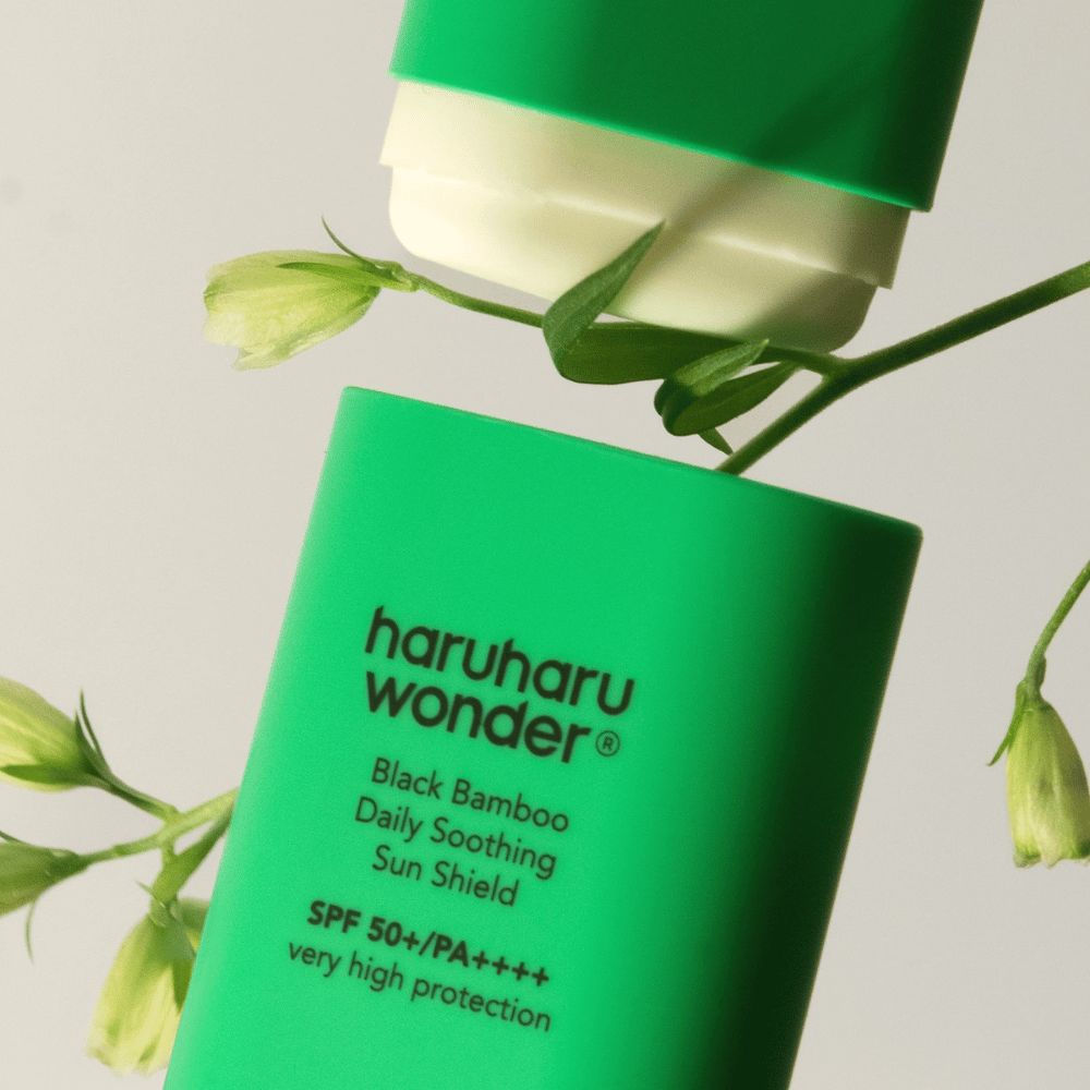 Close-up de Haruharu Wonder Black Bamboo Daily Soothing Sun Shield – um protetor solar verde em formato de bastão com SPF 50+ PA++++, rodeado por detalhes de plantas verdes.