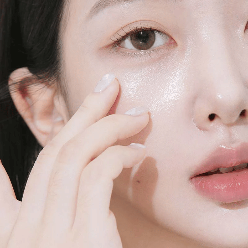 Close de uma mulher aplicando creme de olhos sob o olho com as pontas dos dedos. A pele parece hidratada, brilhante e cuidada com um brilho natural.