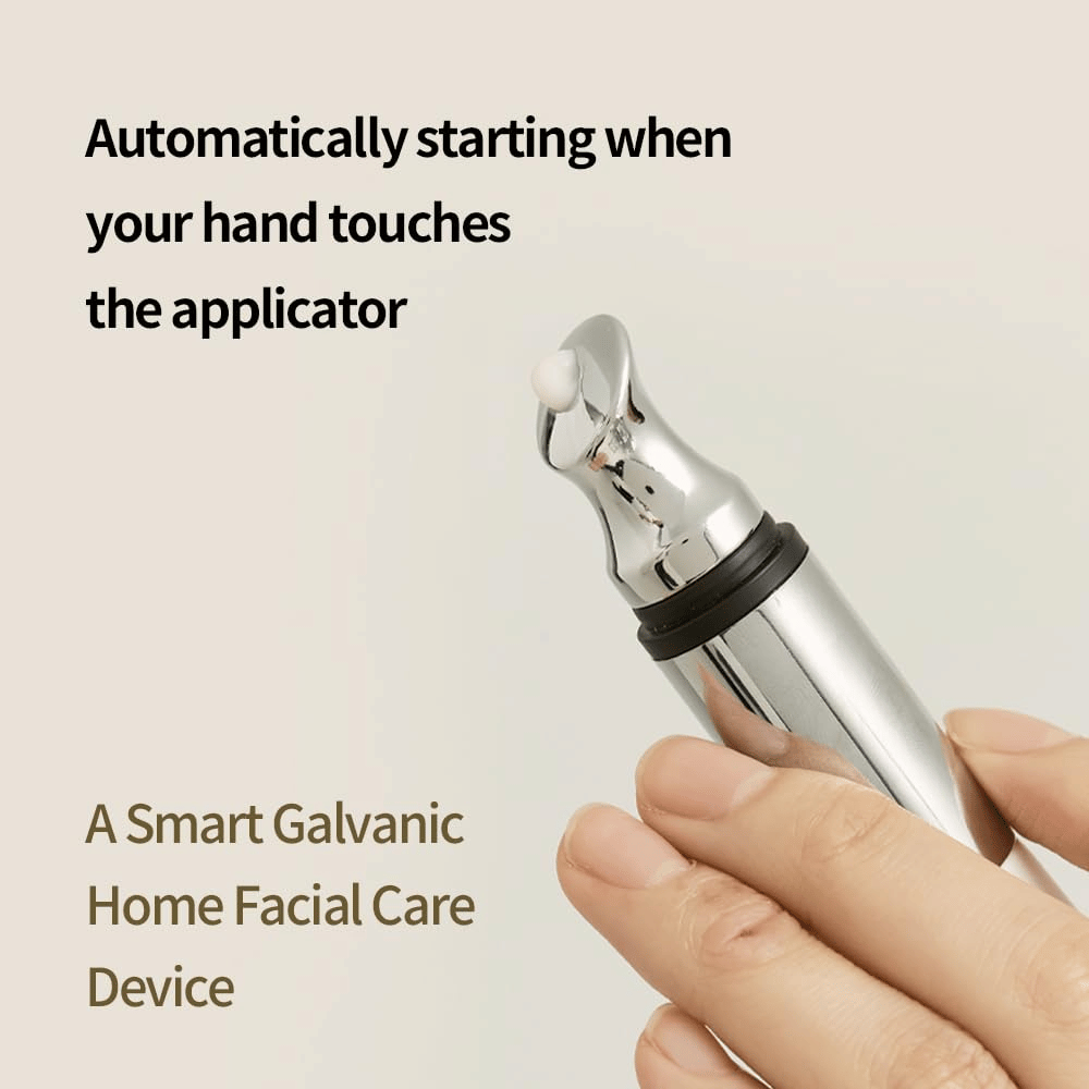 Close de uma mão segurando um aplicador galvânico para creme de olhos com função de início automático ao toque. O texto na imagem descreve a função e o dispositivo como uma ferramenta doméstica inteligente para cuidados faciais.