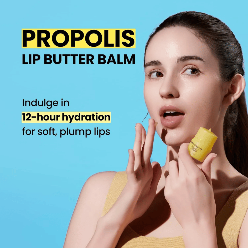Uma mulher aplica CNP Laboratory Propolis Lip Butter Balm, destacada contra um fundo azul. O produto promete 12 horas de hidratação para lábios macios e volumosos, mostrado com um tubo amarelo que ela segura na mão.
