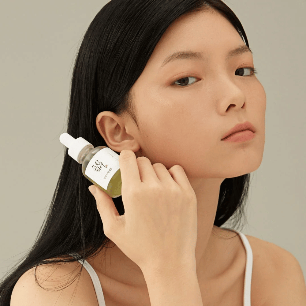 Modelo segurando Beauty of Joseon Calming Serum na bochecha – chá verde e pantenol que fortalece a barreira da pele.