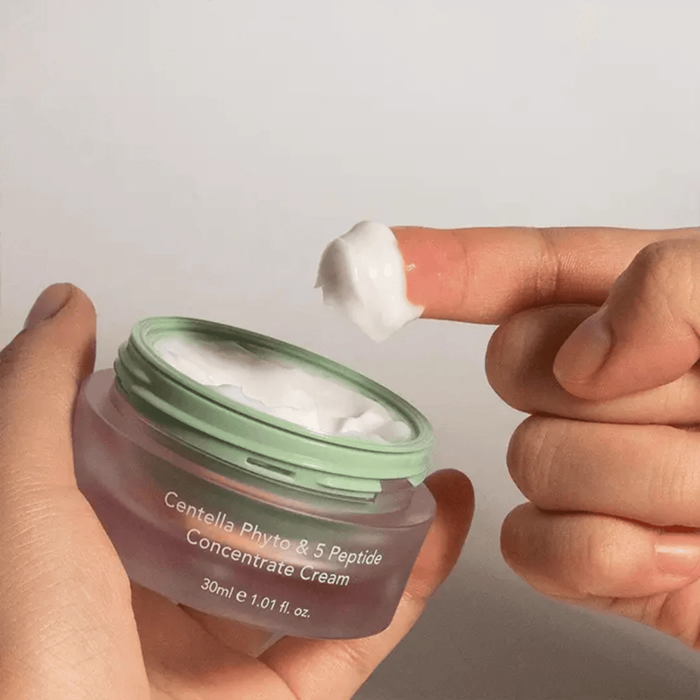 Mão pegando uma porção de Centella Phyto & 5 Peptide Concentrate Cream de um frasco.