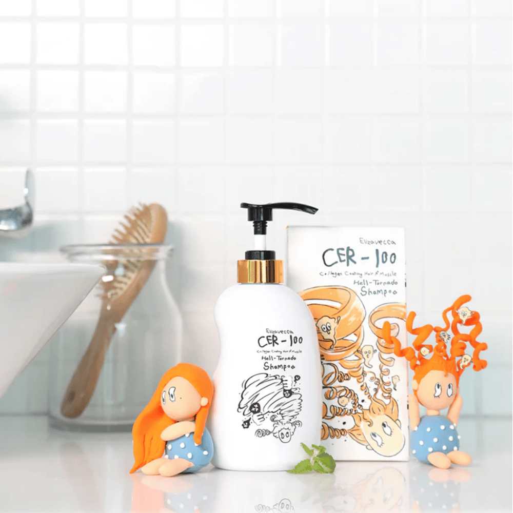 Elizavecca CER-100 Shampoo e a caixa são mostrados num ambiente de casa de banho ao lado de uma escova de cabelo e figuras decorativas. A imagem transmite uma rotina quotidiana de cuidados capilares e a utilização do produto em ambiente doméstico.