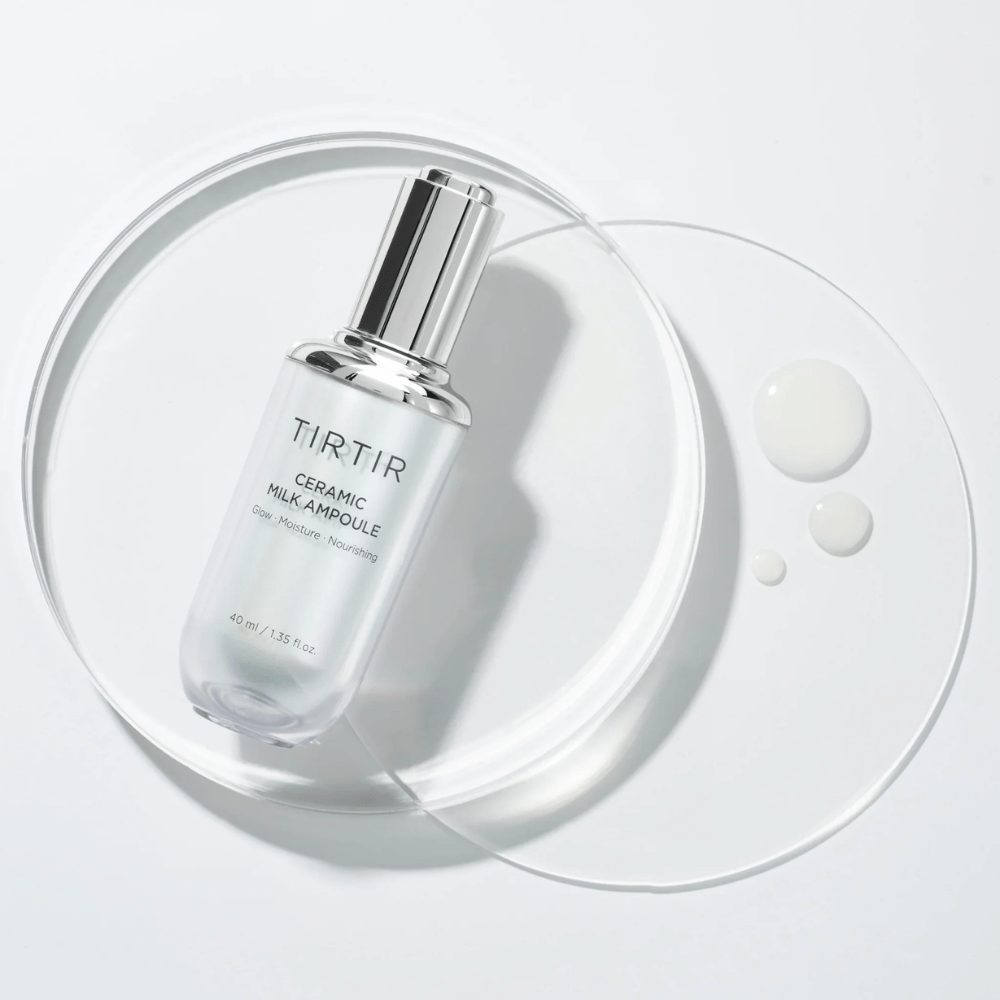 Uma garrafa transparente TIRTIR Ceramic Milk Ampoule em uma placa de vidro com gotas, contra um fundo branco, destaca brilho, umidade e nutrição.