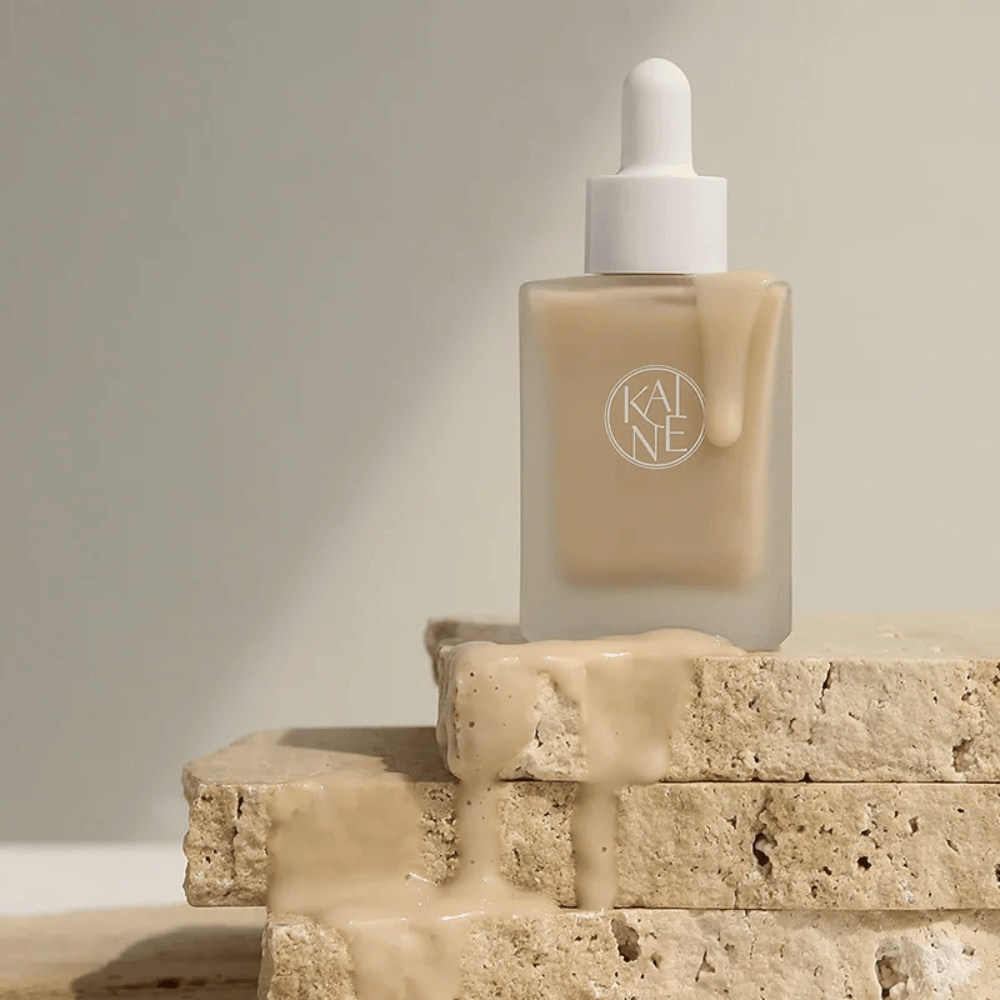 KANE Chaga Collagen Charging Serum em uma garrafa de vidro fosco com pipeta. Textura cremosa escorre sobre pedras naturais em uma luz suave e minimalista.