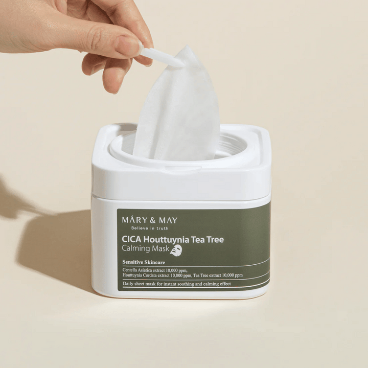 Hand som drar upp en sheetmask ur Mary & May Cica Houttuynia Tea Tree Calming Mask-burk – lugnande ansiktsmask för känslig hud med Cica och Tea Tree-extrakt.