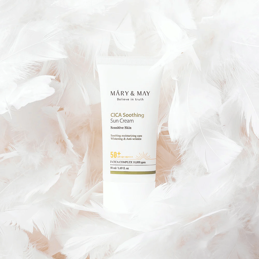 Mary&May CICA Soothing Sun Cream rodeado por suaves penas brancas. A imagem transmite uma sensação de suavidade, conforto e fórmula leve adaptada para pele sensível.