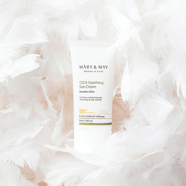 Mary&May CICA Soothing Sun Cream rodeado por suaves penas brancas. A imagem transmite uma sensação de suavidade, conforto e fórmula leve adaptada para pele sensível.