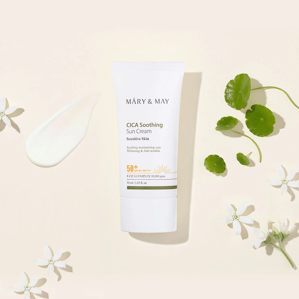 Mary&May CICA Soothing Sun Cream SPF50+ PA++++ apresentada juntamente com uma textura de creme, folhas de centella e flores brancas. A imagem destaca as propriedades calmantes do produto e o foco na pele sensível.