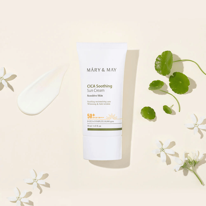 Mary&May CICA Soothing Sun Cream SPF50+ PA++++ apresentada juntamente com uma textura de creme, folhas de centella e flores brancas. A imagem destaca as propriedades calmantes do produto e o foco na pele sensível.