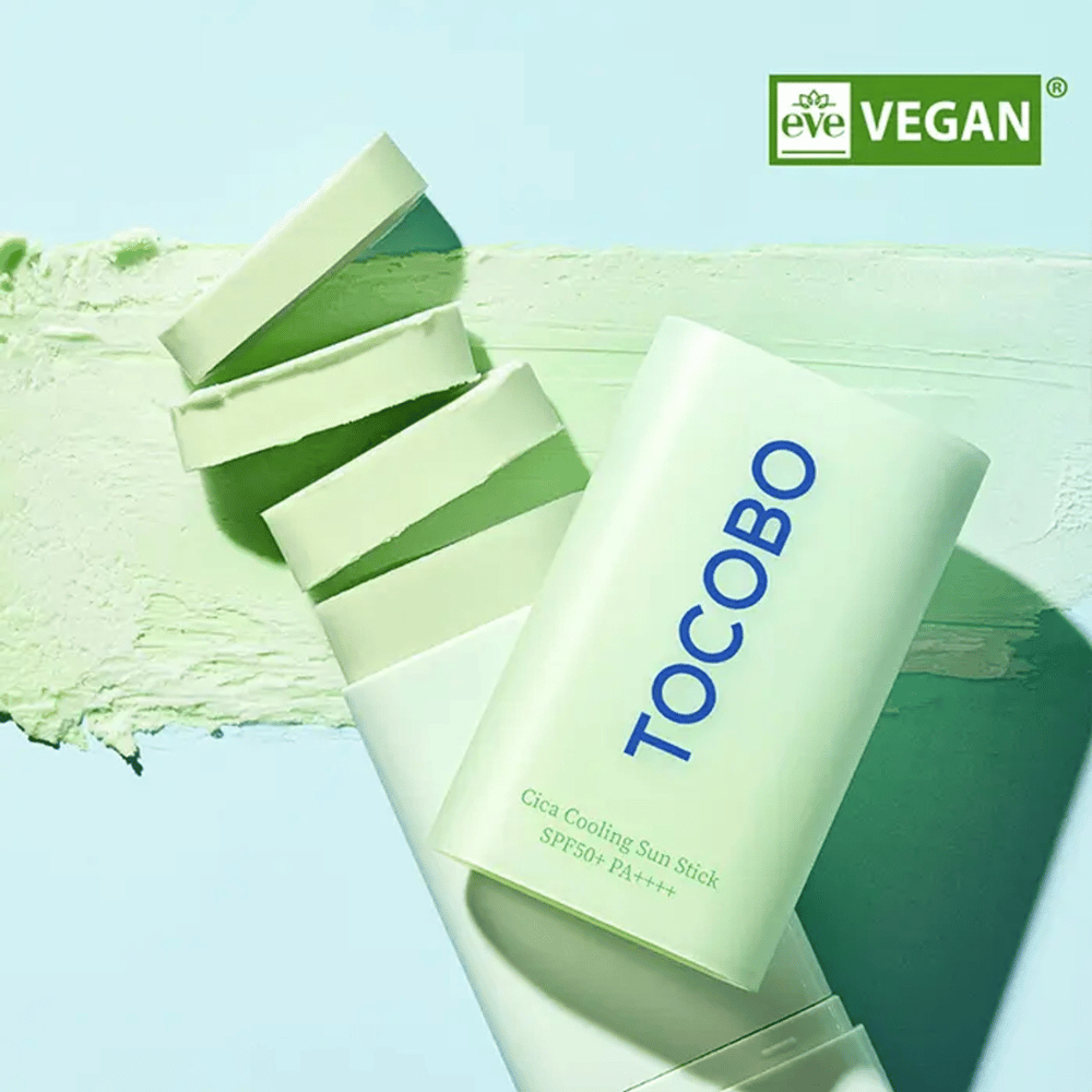 Tocobo Cica Cooling Sun Stick SPF50+ PA++++ em embalagem verde clara com marca de veganismo (EVE VEGAN), deitado sobre uma camada de bastão solar verde.