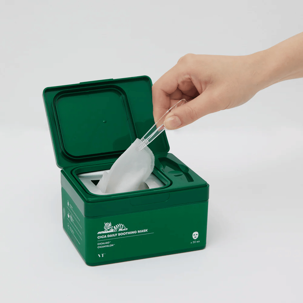 Mão usa uma pinça para pegar uma Sheet mask de um recipiente verde marcado "Cica Daily Soothing Mask".