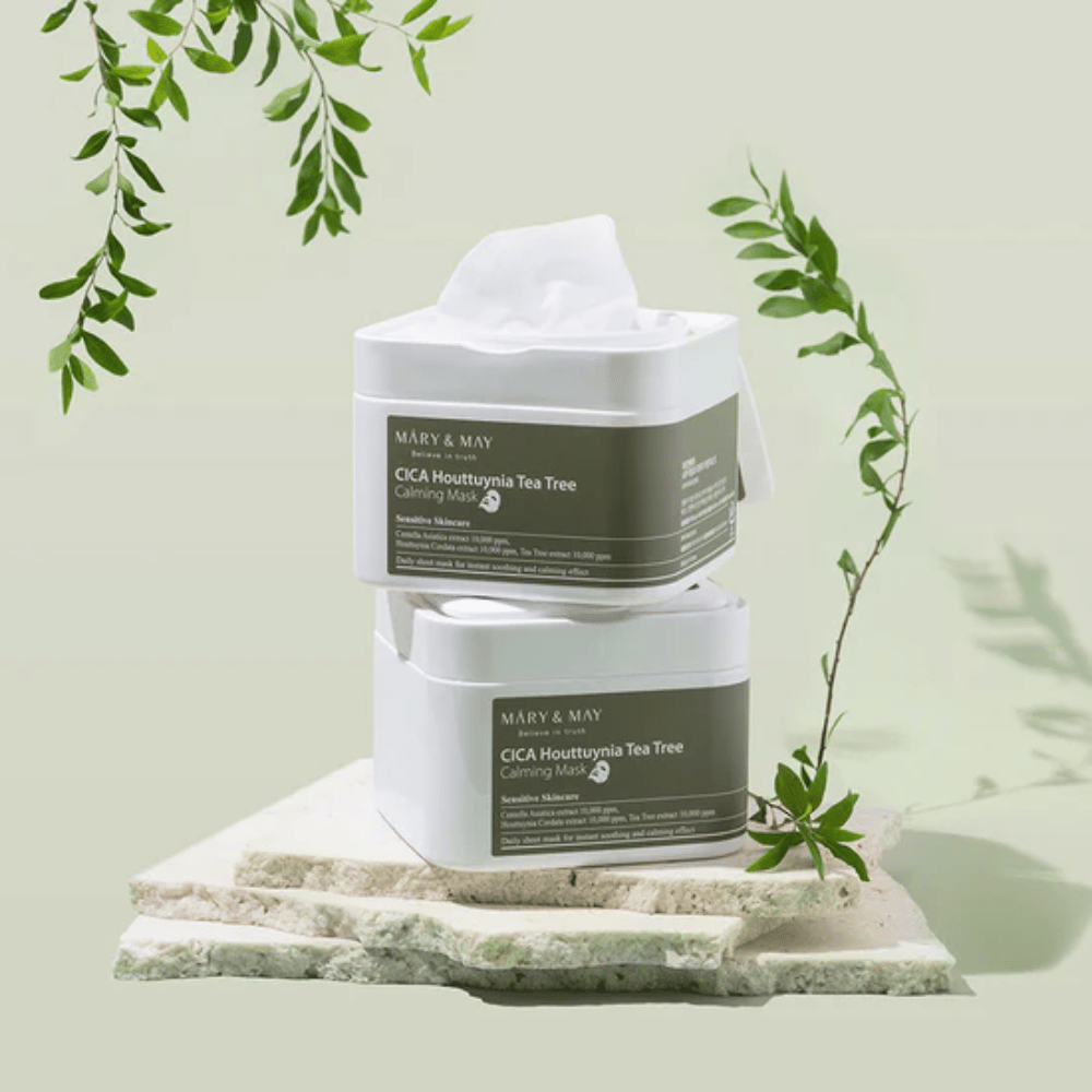 Två burkar Mary & May Cica Houttuynia Tea Tree Calming Mask placerade på natursten med gröna växtdetaljer – lugnande sheetmasker för känslig hud.
