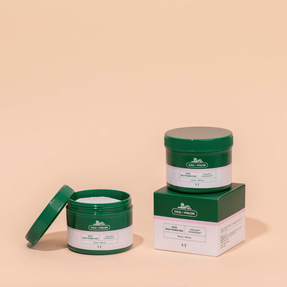Dois frascos verdes com VT Cica Mild Toner Pad, um aberto mostrando as almofadas de toner brancas e outro fechado colocado sobre a sua embalagem de produto, sobre fundo bege.