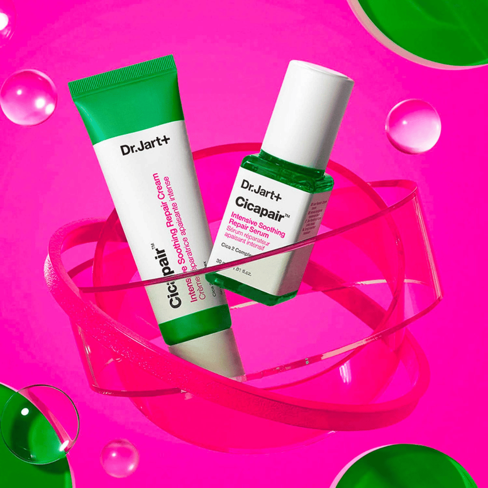 Dr.Jart+ Cicapair Intensive Soothing Repair Cream e Serum em embalagens verdes, que estão sobre uma base circular rosa. Os produtos são desenvolvidos para acalmar e reparar a pele irritada.
