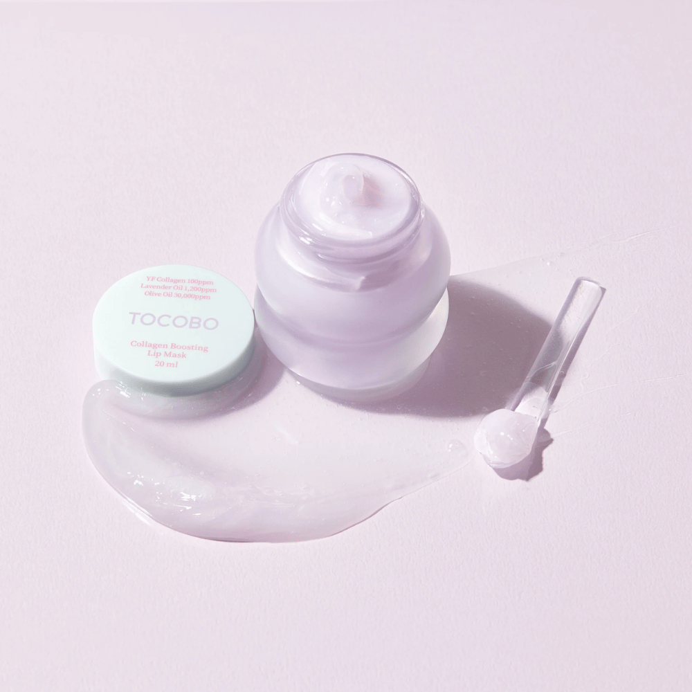 Frasco aberto TOCOBO Collagen Boosting Lip Mask com espátula e creme lilás espalhado sobre fundo lilás claro.