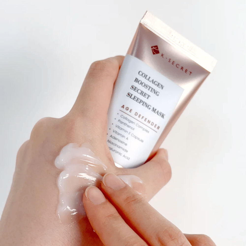 Uma mão segura Collagen Boosting Secret Sleeping Mask enquanto a outra aplica uma quantidade generosa de creme na parte superior da mão – mostrando a consistência e aplicação do produto.