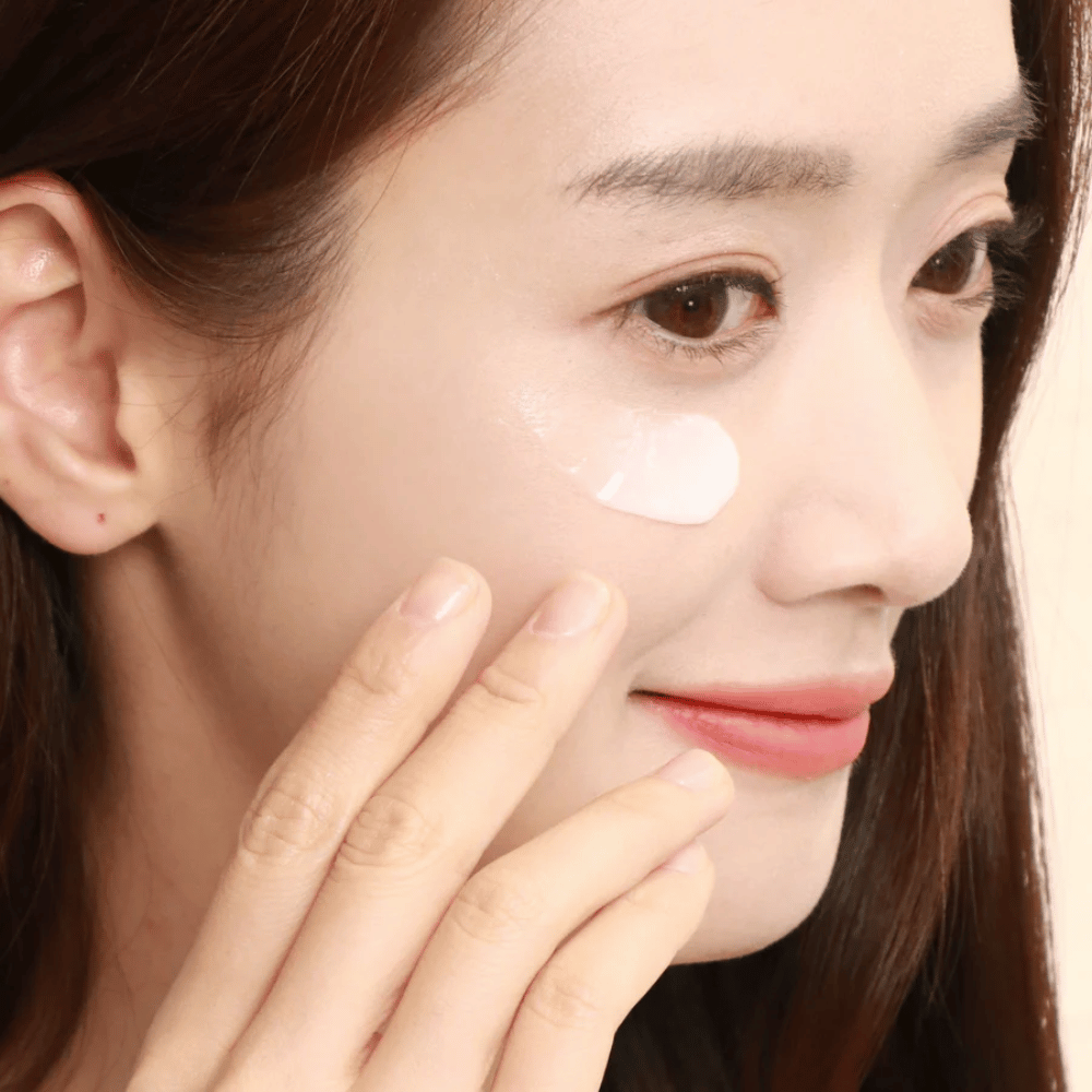 Mulher aplica creme para os olhos sob o olho com as pontas dos dedos – close-up mostrando como o produto é suavemente massageado na pele para hidratação e cuidado.