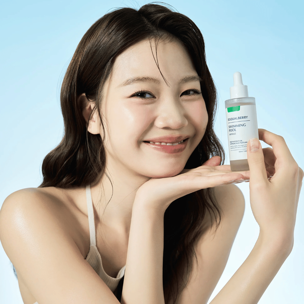 Mulher sorridente segurando Eqqualberry Swimming Pool Ampoule, um produto de cuidados com a pele hidratante, com ambas as mãos em frente a um fundo azul claro.
