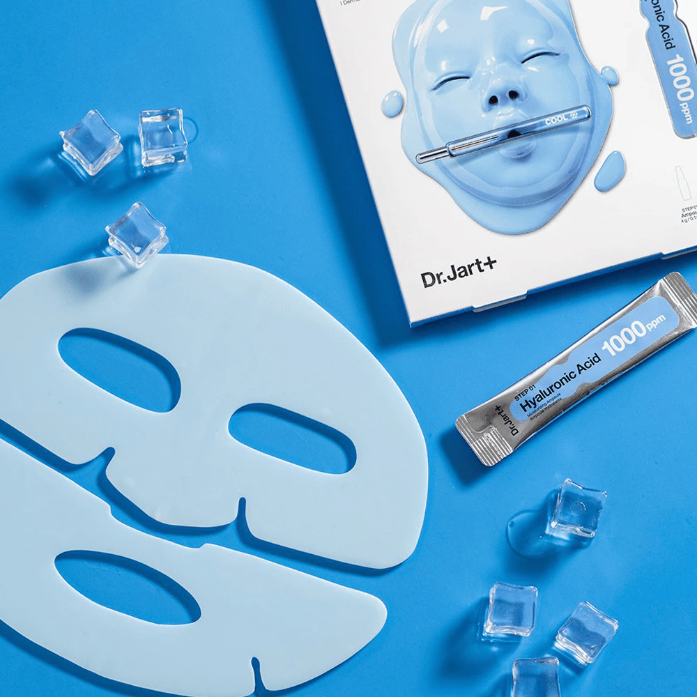 Dr.Jart+ Cryo Rubber Moisturizing Mask com máscara de borracha azul em duas partes, cubos de gelo, ampola de ácido hialurônico e embalagem contra fundo azul.