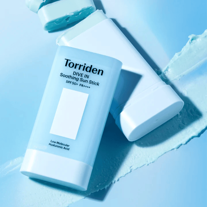 Torriden DIVE IN Soothing Sun Stick SPF50+ PA++++ juntamente com a textura do produto espalhada, ilustrando a aplicação leve e hidratante.