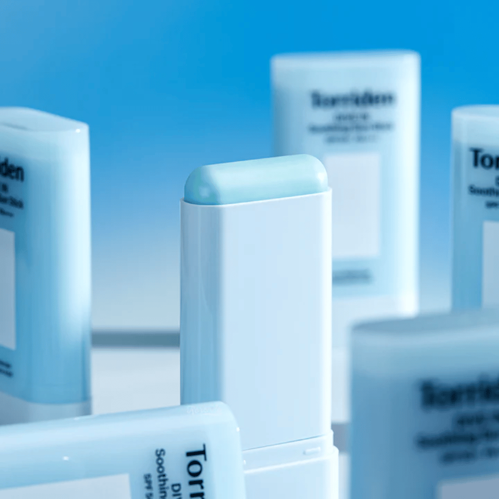 Plano aproximado de Torriden DIVE IN Soothing Sun Stick que mostra a fórmula suave de proteção solar em stick, com vários produtos ao fundo.