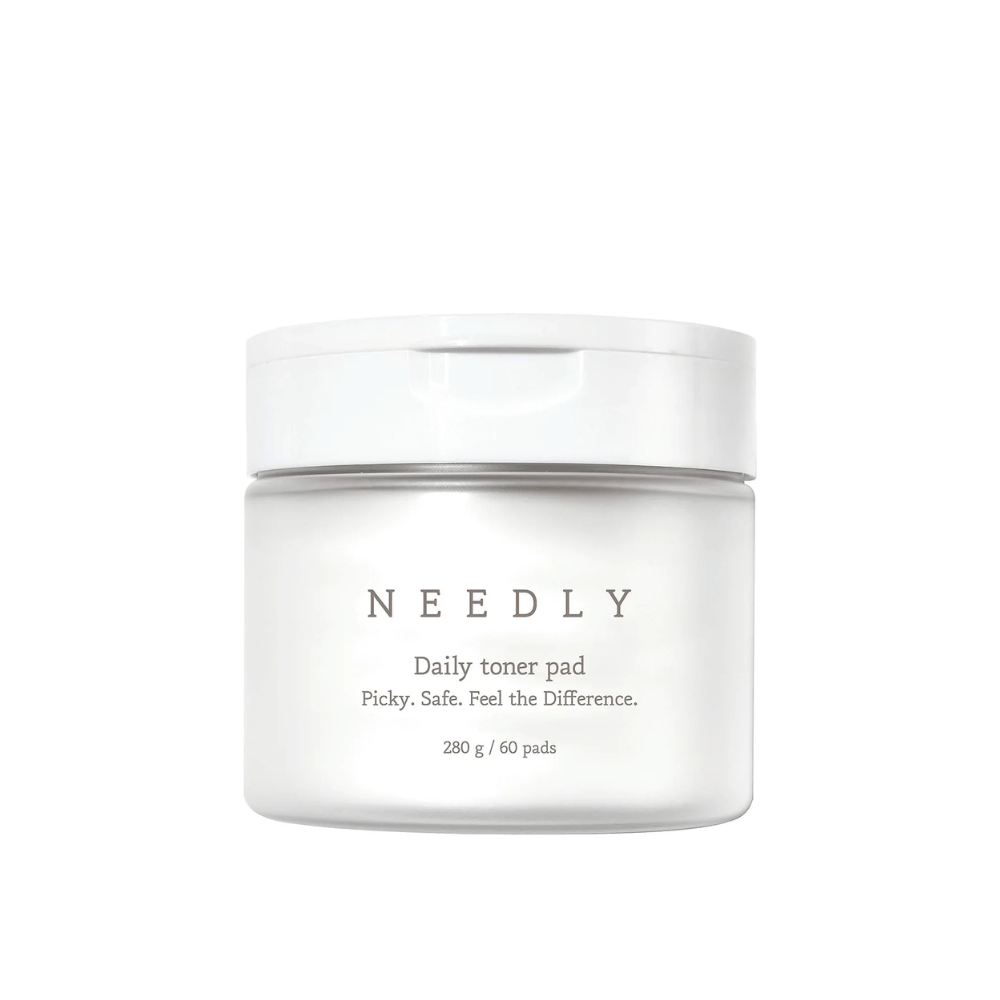 Um frasco branco com Needly Daily Toner Pad. A embalagem tem texto minimalista que descreve o produto e contém 280 g, correspondendo a 60 almofadas de toner. O texto diz 'Picky. Safe. Feel the Difference.